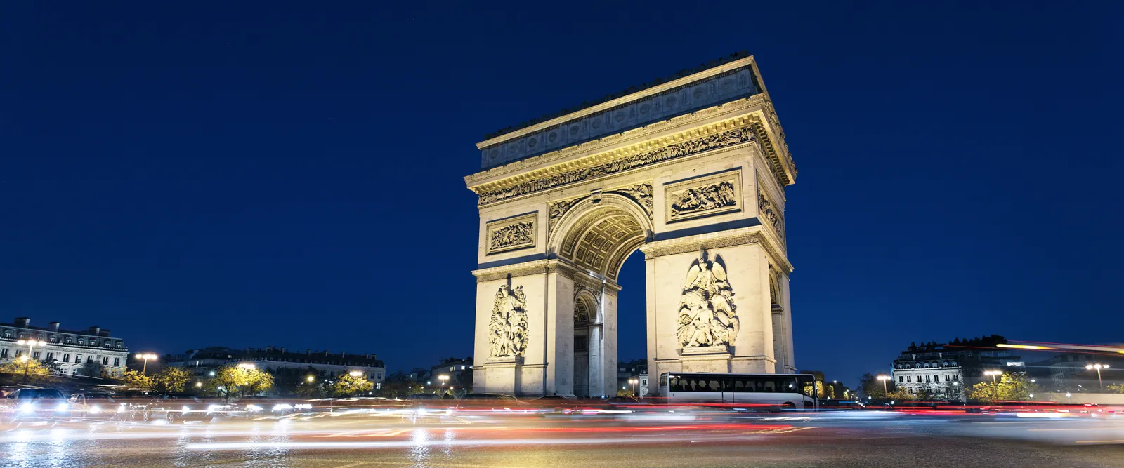 L'Arc de Triomphe illuminé de nuit avec les traînées lumineuses des voitures