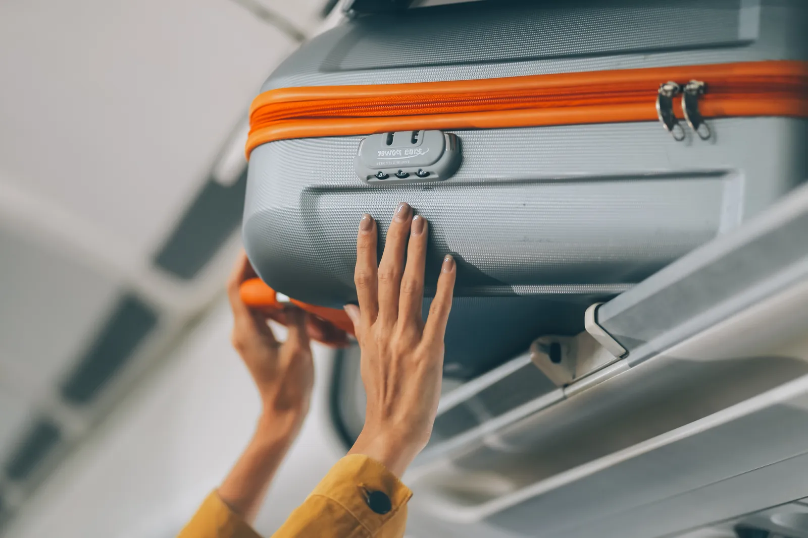 Valise cabine : dimensions et poids par compagnie (tableau) Voyageuse rangeant sa valise cabine dans le coffre à bagages de l'avion