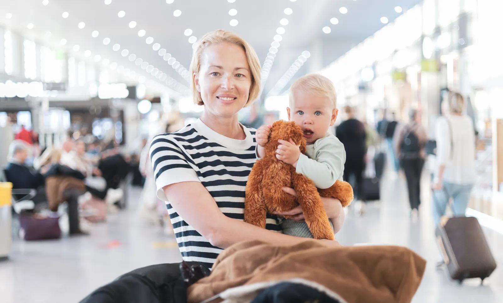 Voyager avec bébé : papiers, avion, santé et destinations Mère portant son bébé dans un terminal d'aéroport avant l'embarquement